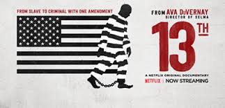 Image of U.S. flag in black and white with stripes blending into stripes on prisoner's uniform. A Black man walking with shackles on his ankles. Text: From Ava Duverney, director of Selma. 13th. A Netflix original documentary. Now streaming.