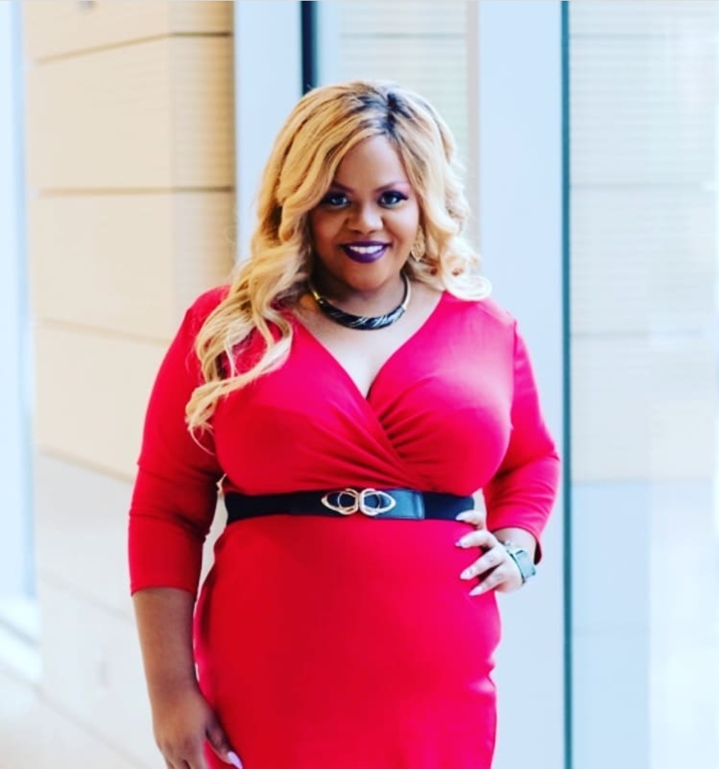 Prenicia Clifton standing and smiling with one hand on her hip wearing a red dress.