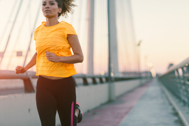 Latina running on a bridge at sunset wearing a bright yellow tee shirt and black pants.