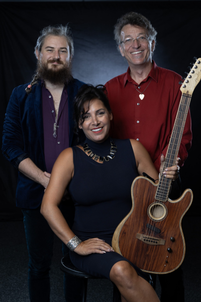 A woman sits with a guitar with two men behind her.
