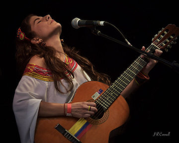 Angela Puerta holds a guitar in front of a microphone