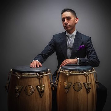 Luis Armacanqui sits with arms resting on two drums
