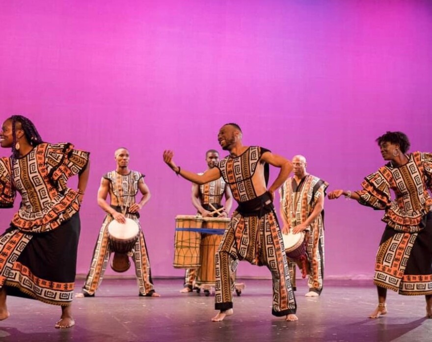 Ko-Thi dancers move around a stage in front of a purple background