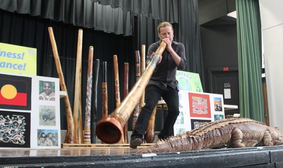 Rob Thomas playing the didgeridoo on stage with posters and props from Australia in background