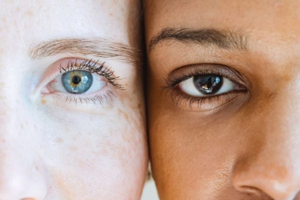 Close up image of two faces pressed cheek to cheek, one with light skin and eyes, the other with dark skin and eyes.