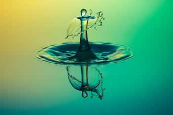 Image of a droplet falling into a pool of water creating a ripple